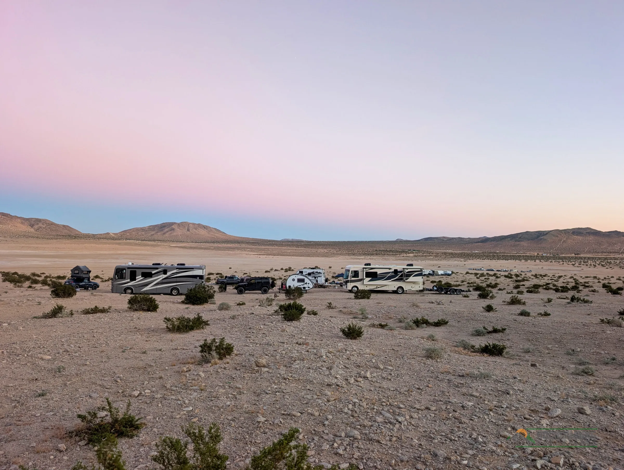 The basecamp on a dry lakebed before sunrise under a pastel sky, mountains on the horizon.