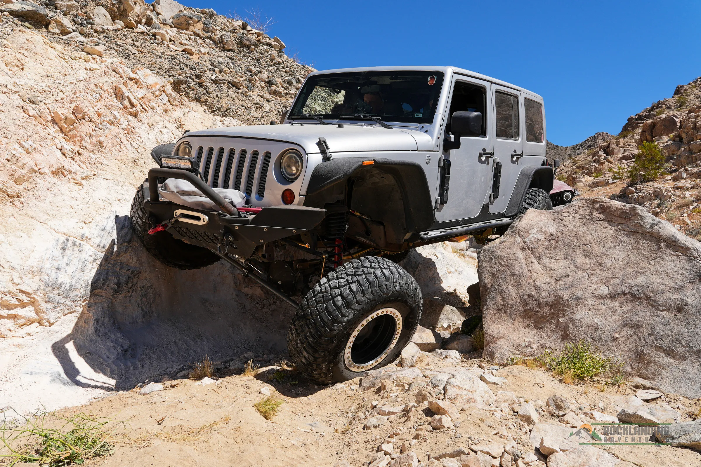 A modified Jeep shows suspension articulation over a rock obstacle.